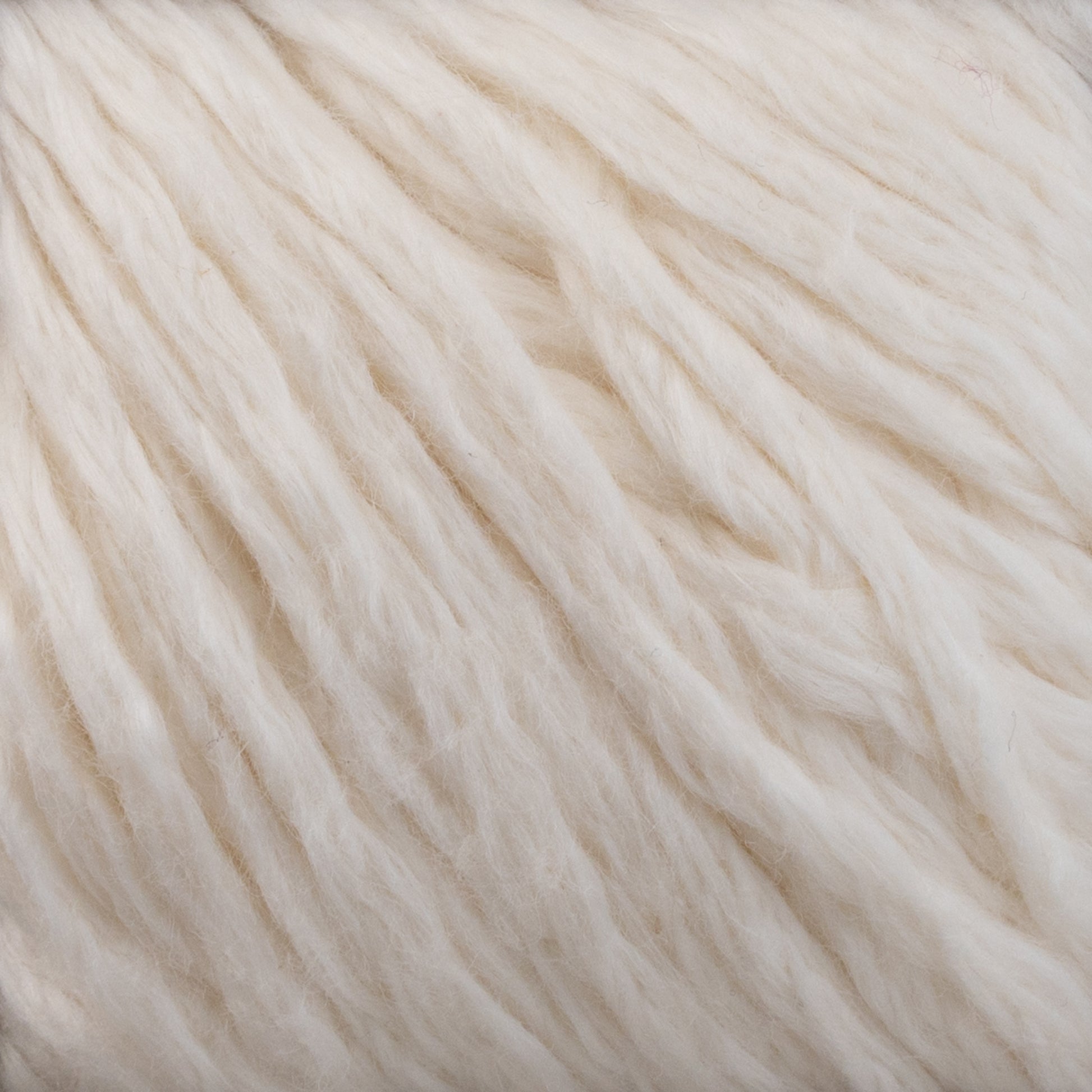 Close-up of soft, ivory-colored Cumulus Cotton by Juniper Moon Farm fibers. The cotton is textured and appears fluffy and thick, with a slightly uneven, natural finish. Its durable chainette construction gives it a warm, cozy feel while being perfect for weightless accessories from Knitting Fever / Euro Yarns.