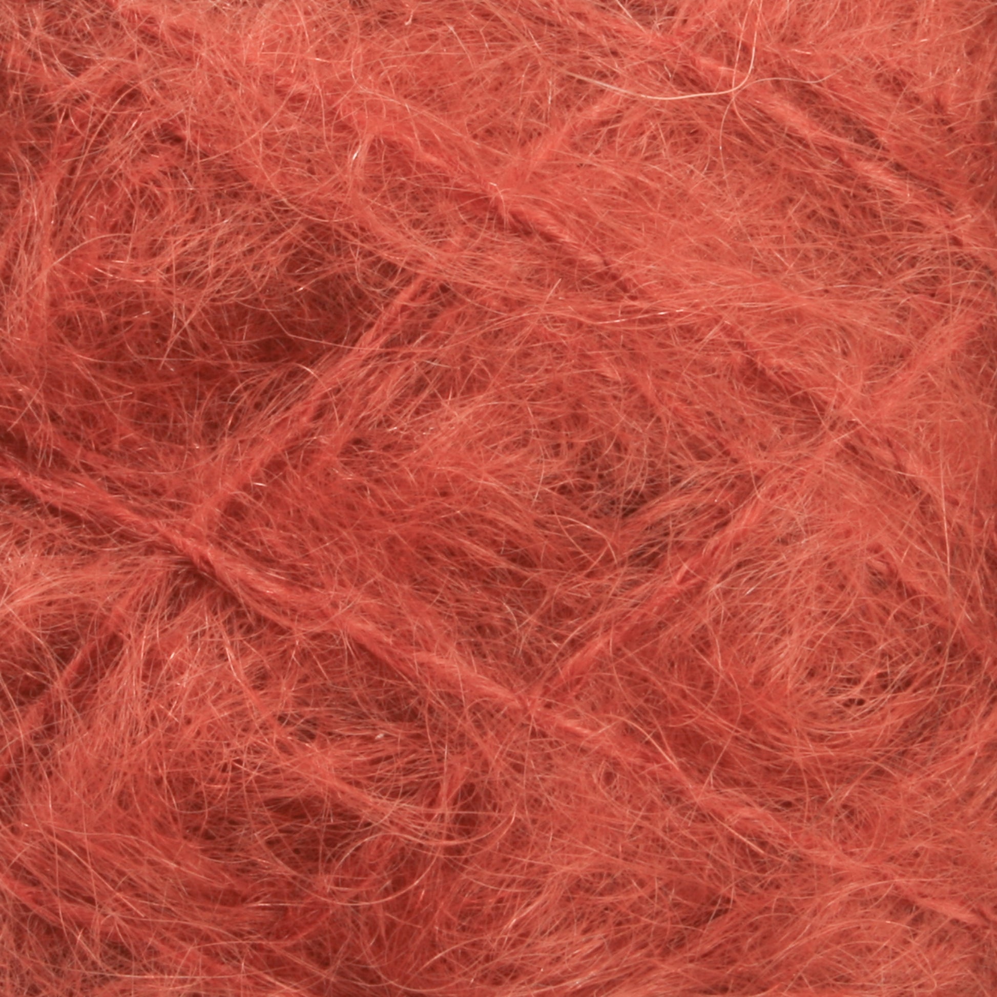 Close-up of a ball of Caledonian Dye Works' Victorian Brushed Mohair Yarn | Mini Skein, showcasing its fluffy and fibrous texture. The strands are interwoven, creating a dense and intricate pattern reminiscent of classic Victorian yarns.