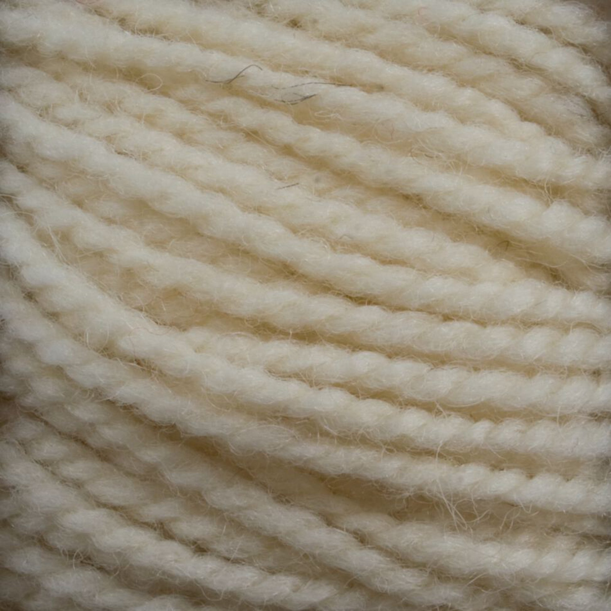 Close-up of a ball of thick, cream-colored Tuffy Canadian Sock Yarn by Briggs & Little. The worsted weight yarn is tightly wound and appears soft and slightly fuzzy, perfect for knitting cozy winter socks. Visible strands and texture highlight the intricate details of this fibrous material.