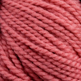 Close-up image of pink yarn. The image shows the texture and color of Norumbega, a product from Caledonian Dye Works. This 100% U.S. wool yarn features thick, twisted strands tightly wound together. Perfect for knitting or crocheting projects, the Aran weight yarn appears soft and thick, suitable for creating warm, cozy items.