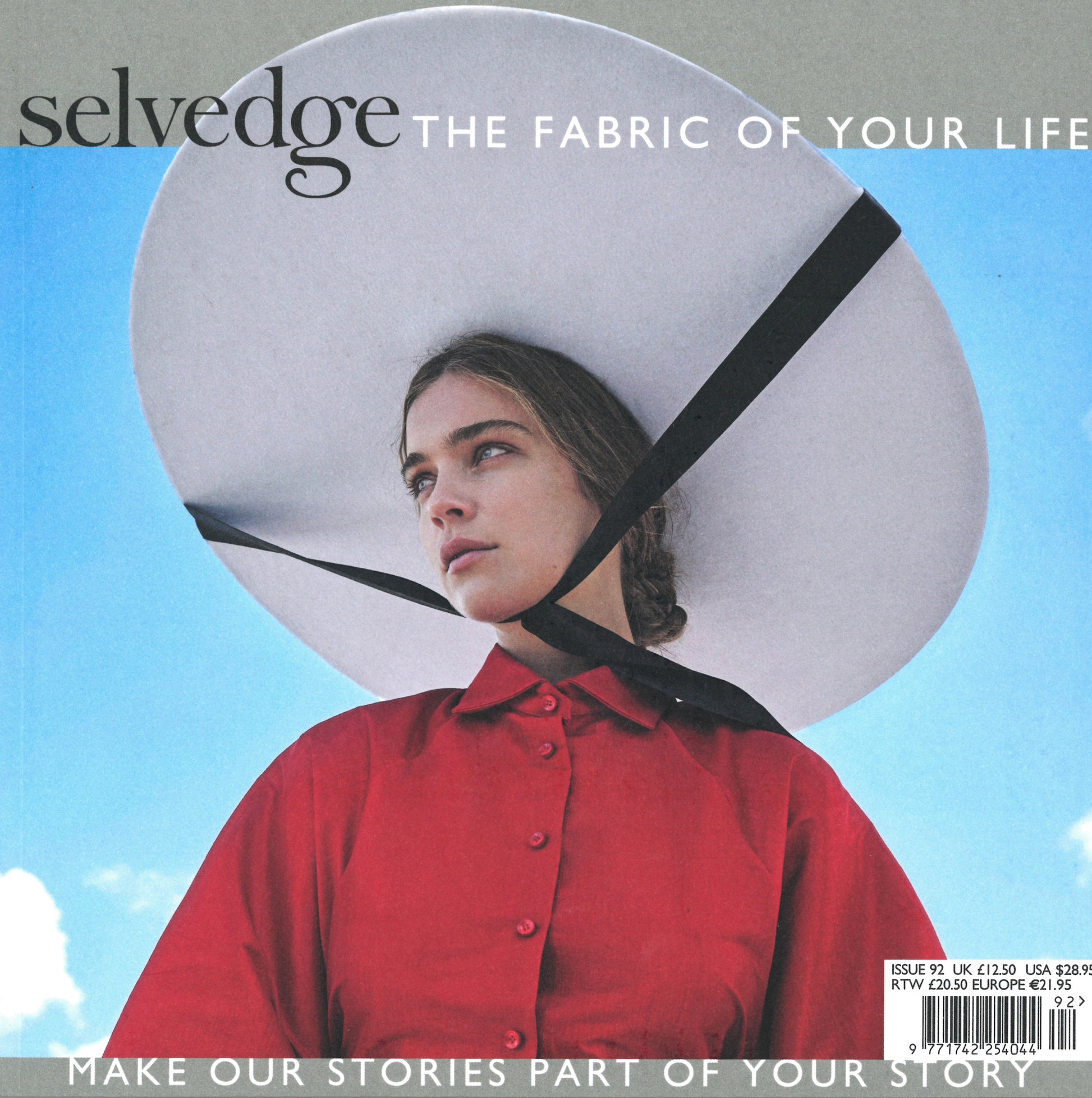 A woman wearing a large white sunhat with a black ribbon and a red button-up shirt gazes into the distance against a blue sky backdrop. The cover text of Selvedge Magazine, Issue 92: Comfort reads "The Fabric of Your Life" and "Make Our Stories Part of Your Story.