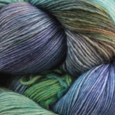 A close-up of Malabrigo Lace by Malabrigo Yarn reveals a skein in various shades of green, blue, purple, and gray. The strands are tightly wound, showcasing its smooth texture and subtle color transitions. The harmonious blend of colors creates an appealing multicolored pattern that's perfect for knitted shawls.