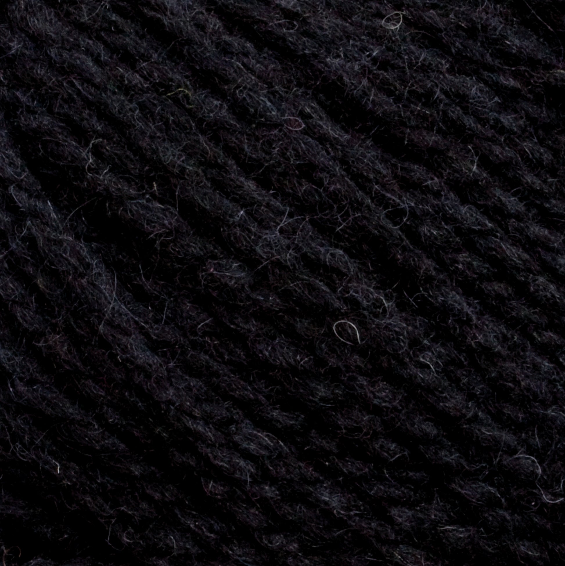 Close-up image of Harrisville Designs' Harrisville Shetland Yarn - Unwashed Cones, showcasing a tightly knitted pattern with visible fibers and texture. The yarn appears soft and woolen, with subtle variations in the shades of black and some loose fibers. Ideal for lightweight blankets or intricate Fair Isle knitting designs.