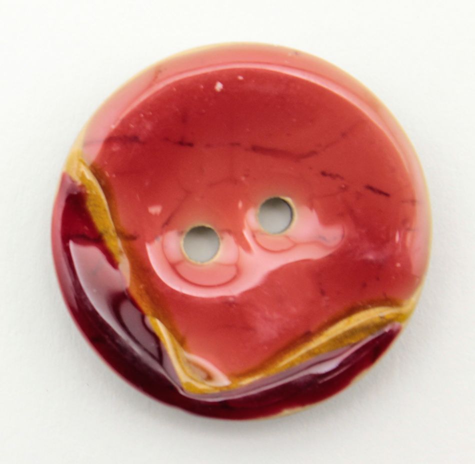 The Coco Boomerang 1 1/8" Button by Buttons Etc. is a round, glossy accessory featuring a marbled design with shades of red, burgundy, and a touch of yellow. It resembles buttons coated with vibrant shellac and has two holes in the center, with a slightly irregular wave-like pattern on its surface. The button is displayed on a plain white background.