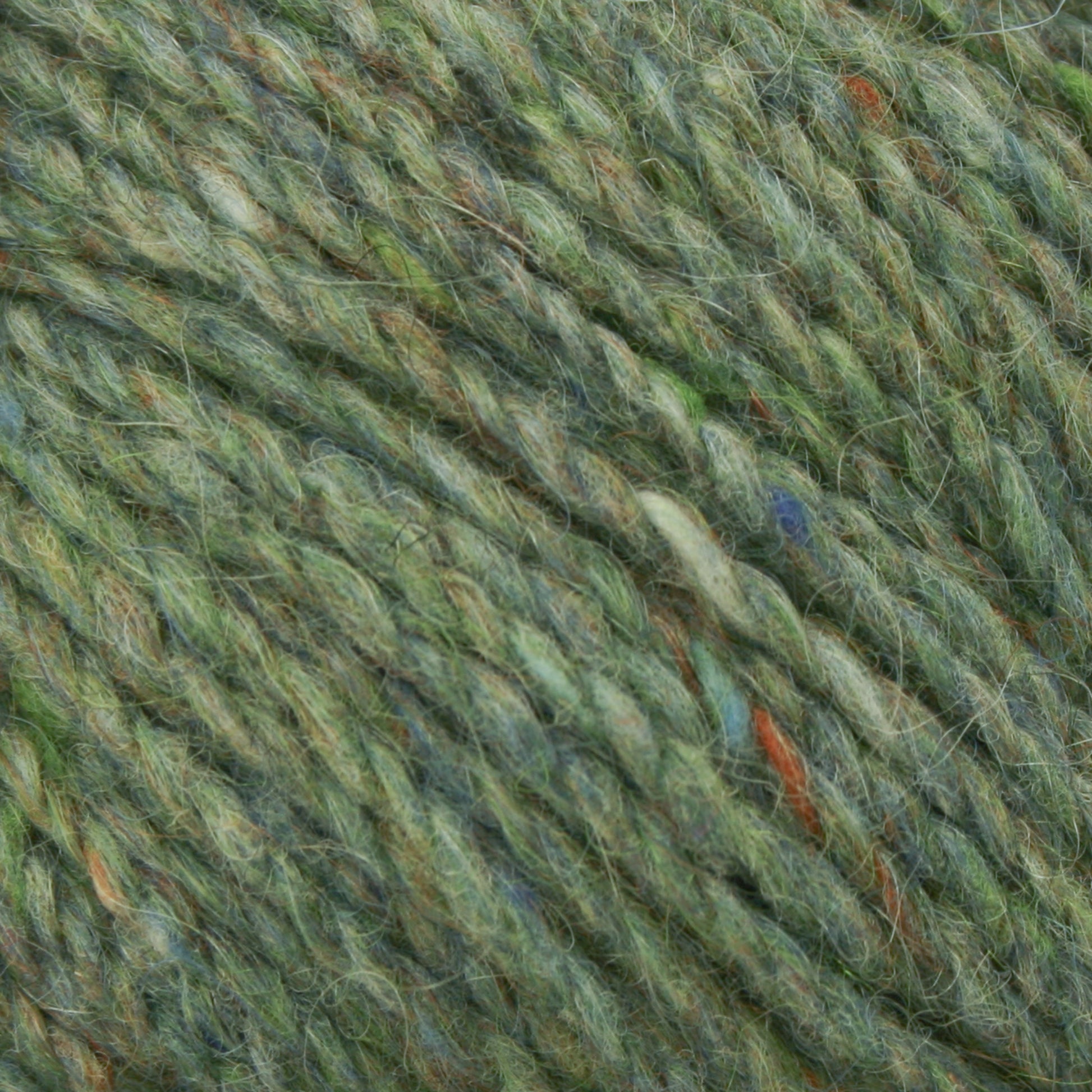 Close-up image of Harrisville Designs' Peace Fleece Yarn showing intertwined fibers in diverse shades of green, accented with flecks of orange, blue, and yellow. The soft and fuzzy texture suggests a blend of wool and mohair, ideal for worsted weight knitting projects.