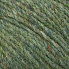 Close-up image of Harrisville Designs' Peace Fleece Yarn showing intertwined fibers in diverse shades of green, accented with flecks of orange, blue, and yellow. The soft and fuzzy texture suggests a blend of wool and mohair, ideal for worsted weight knitting projects.