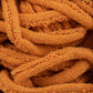 Close-up of a tangled mass of orange Harrisville Potholder Loops from the Friendly Loom's Traditional Size Mini Pack. The texture reveals the intricate knit pattern, with individual loops and stitches visible, reminiscent of work done on a traditional loom. The yarn appears thick and woolly, creating a cozy and warm impression.