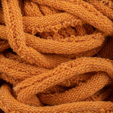 Close-up of a tangled mass of orange Harrisville Potholder Loops from the Friendly Loom's Traditional Size Mini Pack. The texture reveals the intricate knit pattern, with individual loops and stitches visible, reminiscent of work done on a traditional loom. The yarn appears thick and woolly, creating a cozy and warm impression.