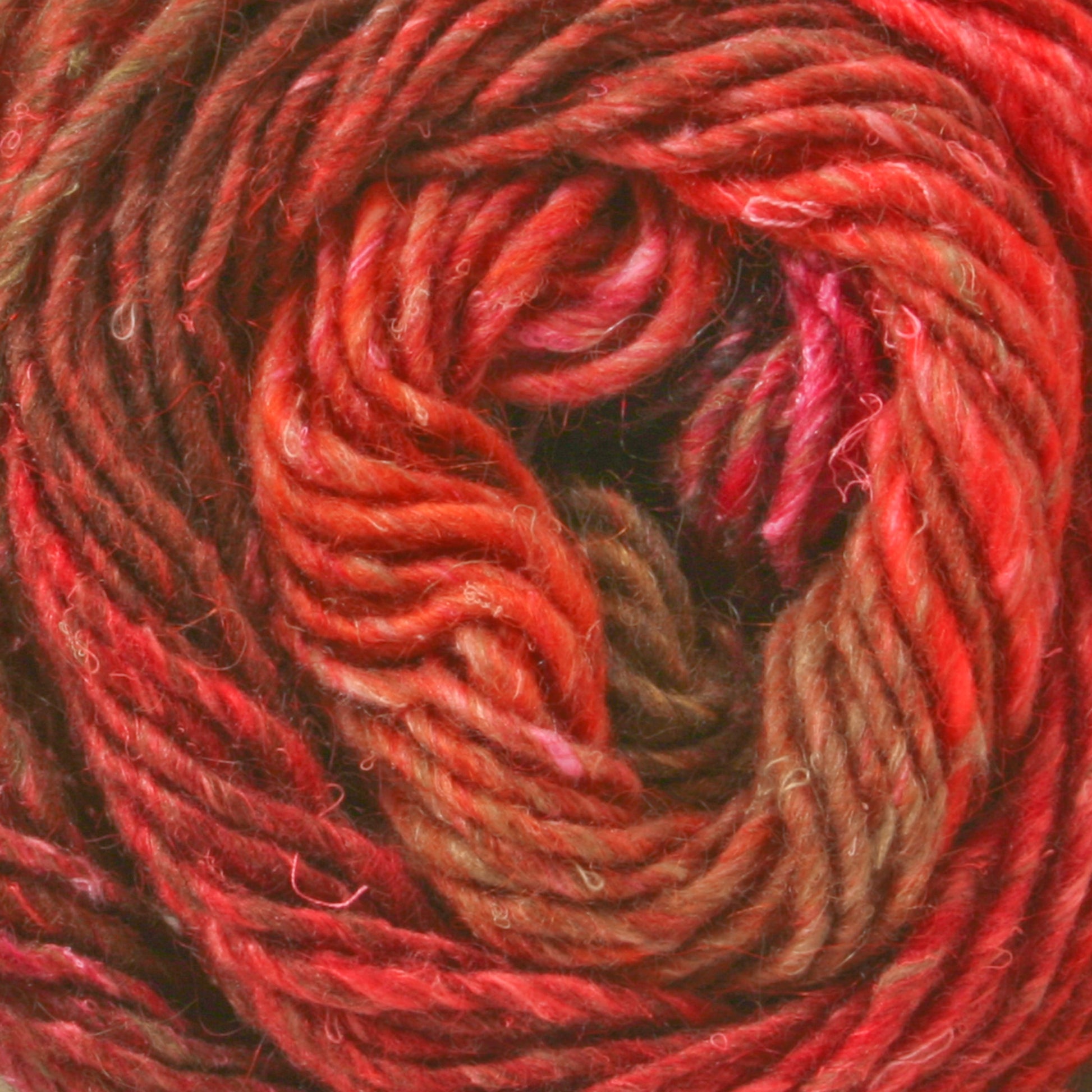 Close-up of a ball of Noro Silk Garden yarn by Knitting Fever / Euro Yarns. This silk and wool blend yarn features a stunning array of multicolored shades, including red, orange, pink, and brown. The visually rich and textured spiral pattern is highlighted by the thick and slightly fuzzy fibers, which showcase the intricate twists of the threads.