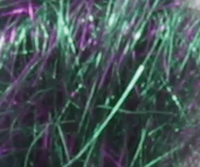 Close-up view of *Clearance! Crystal Mylar Fiber* from Foxglove Fiberarts Supply, showcasing iridescent threads or fibers in shades of green and purple that intertwine with shimmering highlights, reflecting light to create a vibrant, dazzling effect.