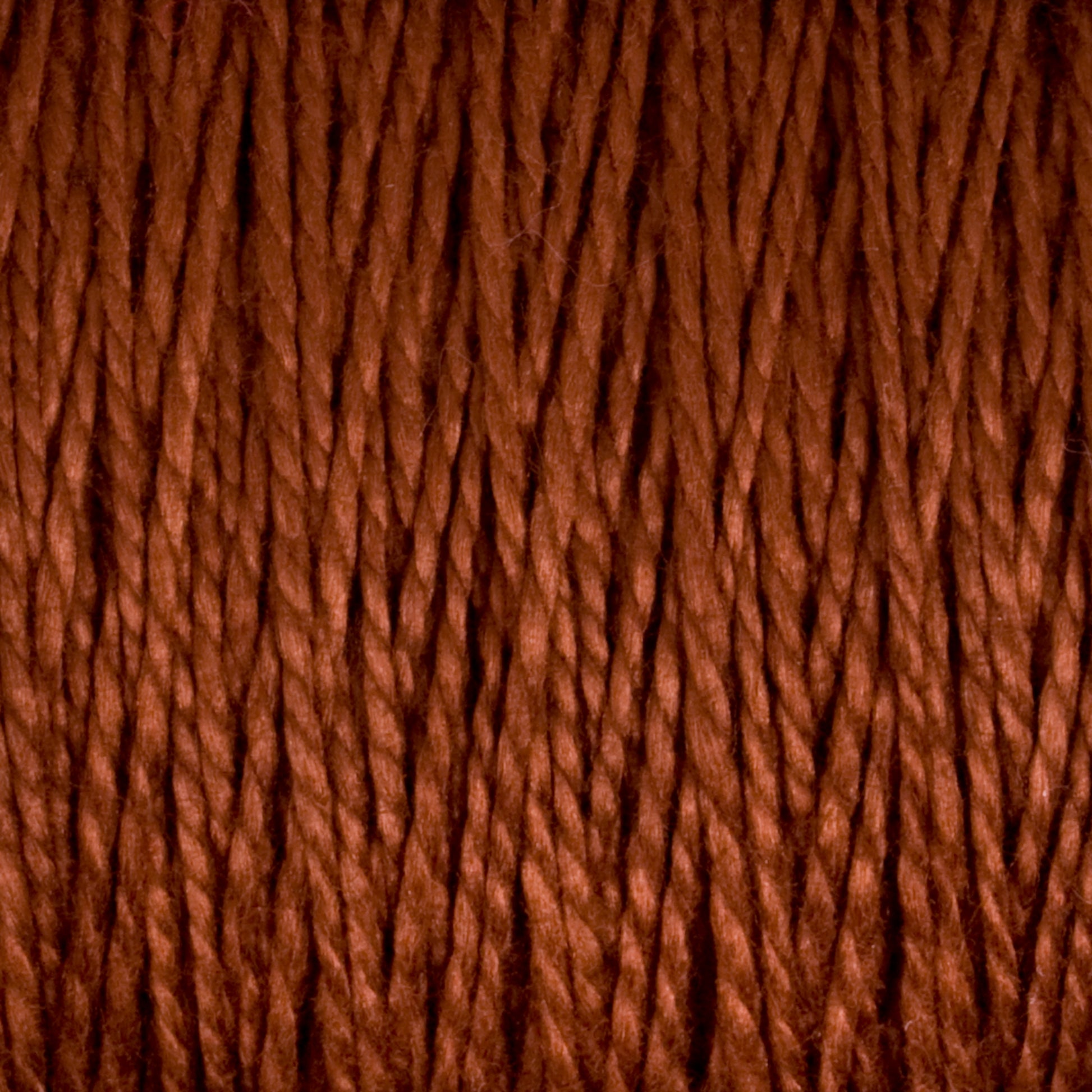 Close-up image of densely packed, twisted strands of dark reddish-brown 10/2 Pearl Cotton Yarn | Mini-cone by Supreme Corp. The texture appears soft and slightly fuzzy, with individual fibers clearly visible, showcasing its excellent colorfastness.