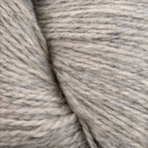 Close-up of light gray, textured Patagonia Organic Merino by Juniper Moon Farm yarn, showcasing its soft fibers and subtle variations in color. The knitting and weaving yarn from Knitting Fever / Euro Yarns is coiled, and the individual threads are discernible, highlighting its fluffy and slightly fuzzy texture.