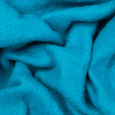 A close-up view of textured, vibrant turquoise fabric with soft, fuzzy fibers and gentle folds shows a plush and cozy material. It resembles Europa Wools Ltd's Merino Prefelt used in felting projects, showcasing a slightly wavy pattern created by the natural flow of the fabric.