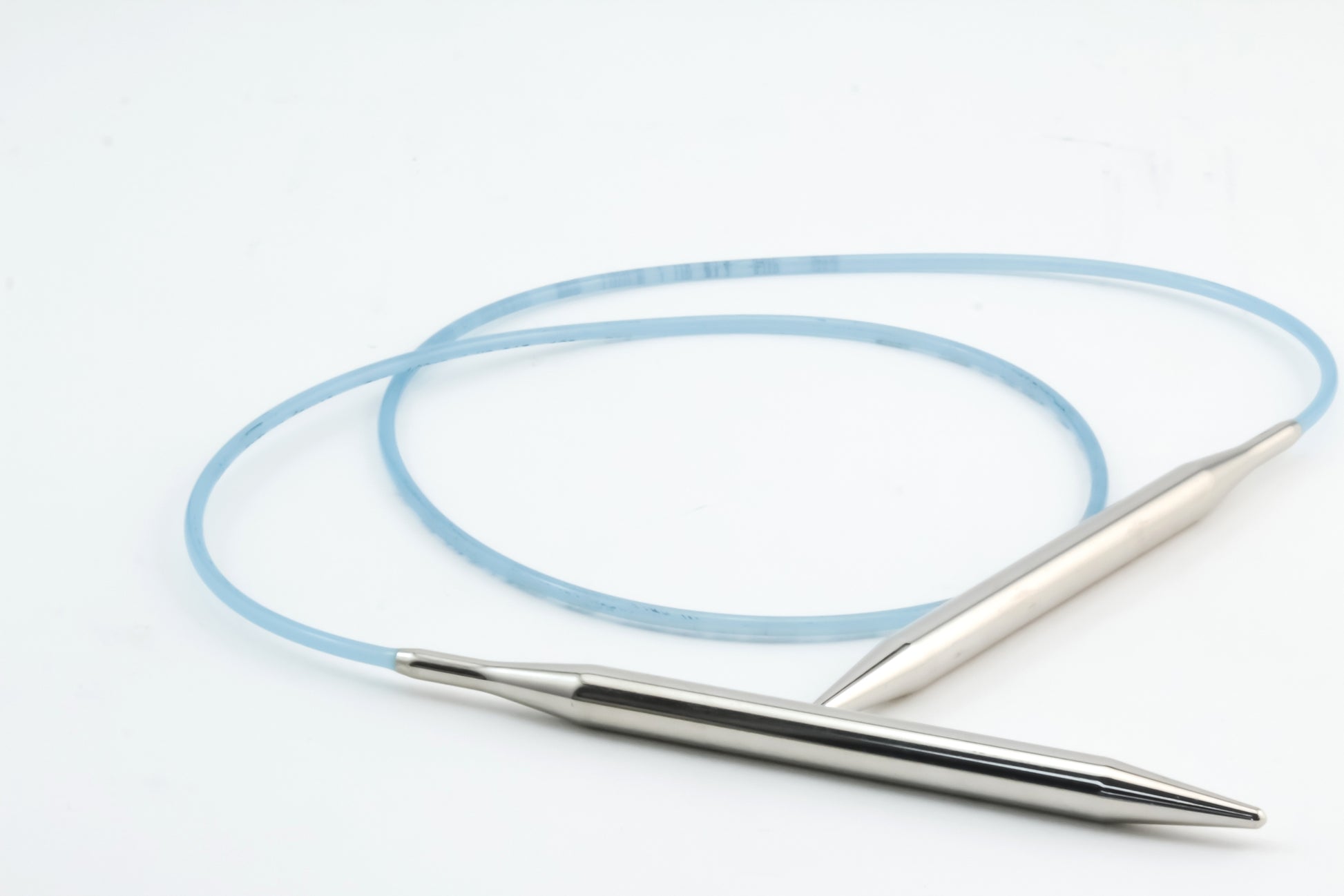 A jump rope with sleek, metallic handles and a light blue cable is coiled on a plain white surface. The design is minimalist and modern, reminiscent of Skacel's Addi Turbo Circular Knitting Needles, featuring smooth, tapered handles that feel just right in your hands.