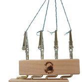 The Leclerc Quad Fringe Twister by Leclerc Looms is a wooden block adorned with a logo and features four adjustable metal clips attached on top using strings. The block also has three brass hooks on the bottom for hanging additional items. The strings on the top are tied together to form a loop, allowing for convenient hanging of the entire device.