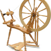 The Kromski Symphony Spinning Wheel by Kromski North America is a Saxony style wooden spinning wheel featuring a large wheel and various intricately carved components such as a treadle, flyer, and bobbins. Designed for spinning thread or yarn from fibers, it showcases a traditional design with a natural wood finish.