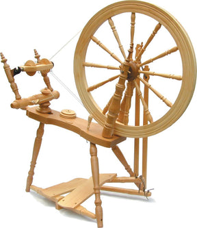 The Kromski Symphony Spinning Wheel by Kromski North America is a Saxony style wooden spinning wheel featuring a large wheel and various intricately carved components such as a treadle, flyer, and bobbins. Designed for spinning thread or yarn from fibers, it showcases a traditional design with a natural wood finish.