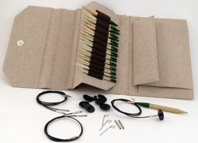 A beige fabric case is open, displaying a set of Lykke Interchangeable Circular Bamboo Knitting Needles from Knitting Fever / Euro Yarns, with brown and green tips neatly arranged inside. In front of the case, various knitting accessories, including cables, stoppers, and keys from the 5" interchangeable knitting needle set, are laid out on a white surface.