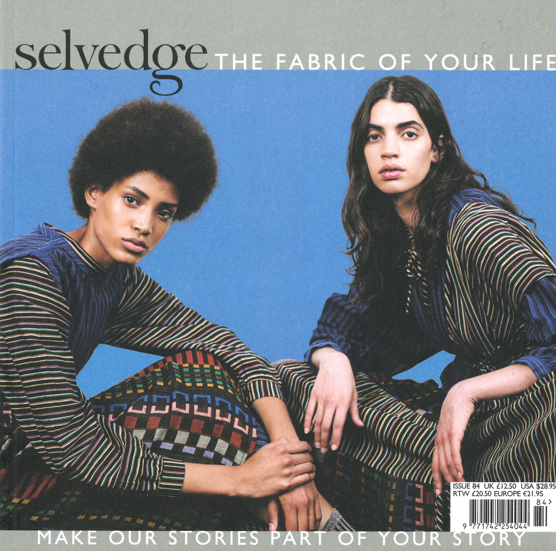 On the cover of Selvedge - Issue 84: Surface; Feel Good Fabrics, two models pose in patterned clothing against a muted blue backdrop. The tagline "The Fabric of Your Life" accompanies the scene, while text at the bottom invites readers to "Make our stories part of your story," highlighting Selvedge's dedication to influencing your fashion journey. A barcode is present on the bottom right corner.