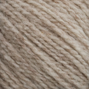 Close-up of a ball of Harrisville Highland - Cones wool yarn by Harrisville Designs in beige and off-white shades, showcasing its soft and fluffy texture with interwoven fibers. The strands appear thick and slightly variegated, highlighting the natural tones and details of the unscoured yarn.