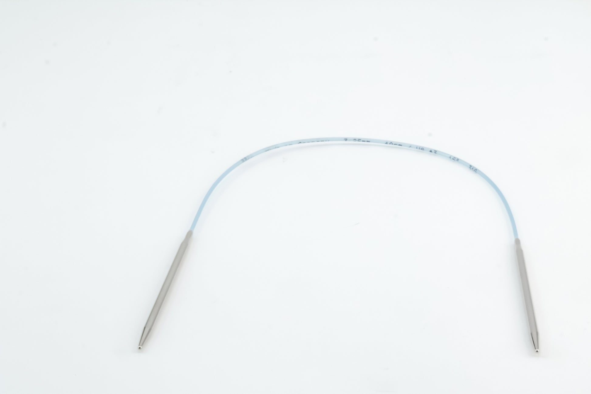 An image of the Addi Turbo Circular Knitting Needles by Skacel shows metallic cylindrical tips at both ends, connected by a blue, flexible shaft reminiscent of short circular needles. The knitting needles are coiled to form an arch shape against a plain white background.