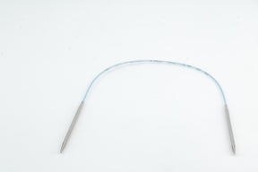 An image of the Addi Turbo Circular Knitting Needles by Skacel shows metallic cylindrical tips at both ends, connected by a blue, flexible shaft reminiscent of short circular needles. The knitting needles are coiled to form an arch shape against a plain white background.