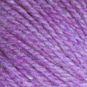 Close-up image of Bartlettyarns Maine Wool Yarn in purple, showcasing its soft, fluffy texture with intertwined strands. The fibers appear thick and cozy, blending heathered colors of purple and lilac tones. The detailed texture emphasizes the plush quality of this worsted weight yarn from Bartlettyarns.