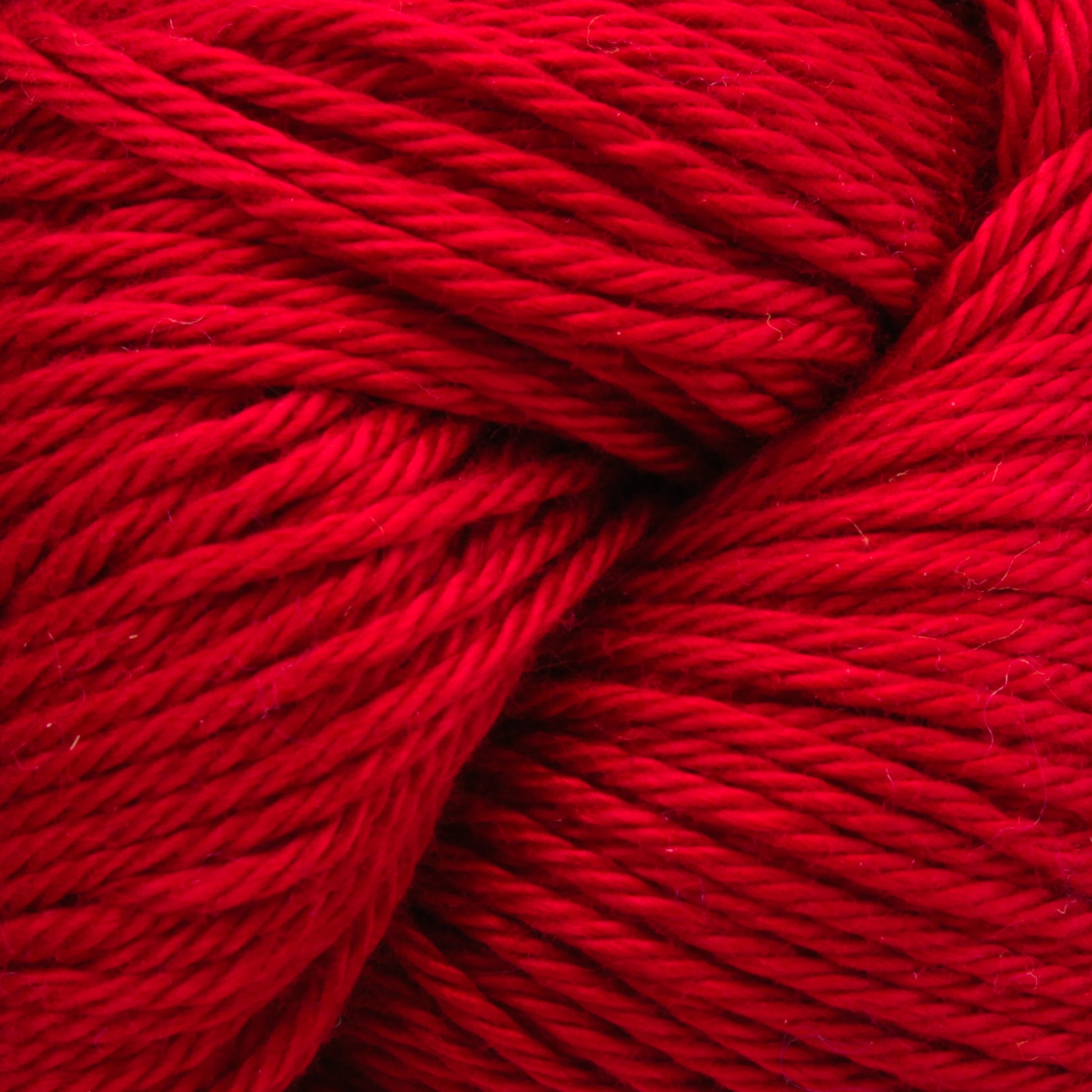 Close-up image of red yarn made from Cascade Ultra Pima Cotton Yarn by Cascade Yarns, showing the tightly twisted fibers and vibrant color. The texture is detailed, highlighting the softness and thickness of the yarn strands, offering a soft hand ideal for any project.