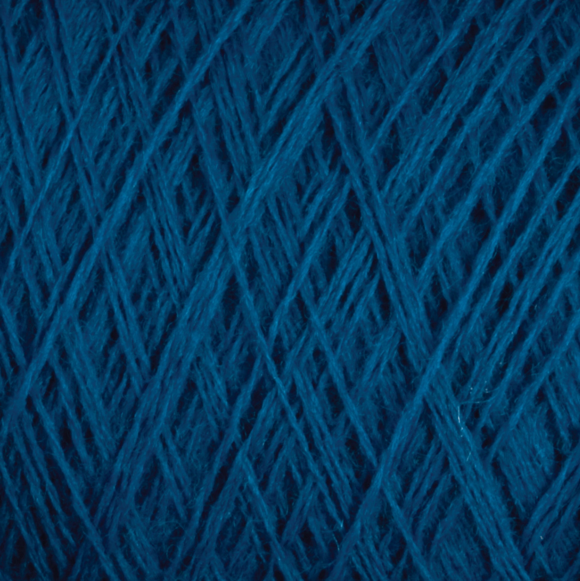 Close-up of tightly wound JaggerSpun Maine Line 3/8 Yarn | Large Cone from Jagger Brothers, Inc., showing the intricate crisscross pattern of the threads. The texture is soft and fibrous, with subtle variations in the hue of the blue strands. The image highlights the detailed structure of this soft, medium grade wool.