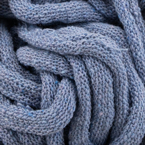 A close-up of a soft, chunky blue knitted fabric showcases intertwined strands that evoke the intricate design created using Harrisville Potholder Loops from the Friendly Loom Traditional Size Mini Pack. The yarn is tightly woven, highlighting its detailed knitting pattern and plush texture, resulting in a textured, cozy appearance reminiscent of handcrafted potholders.