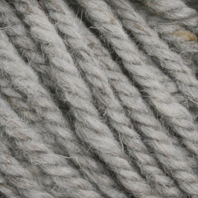 Close-up image of several gray twisted strands of Halcyon Yarn Classic Rug Wool | Skein by Caledonian Dye Works. The texture appears coarse and flecked with lighter and darker fibers, giving the yarn a slightly rustic look akin to what weavers might appreciate. The strands are tightly coiled and densely packed together.