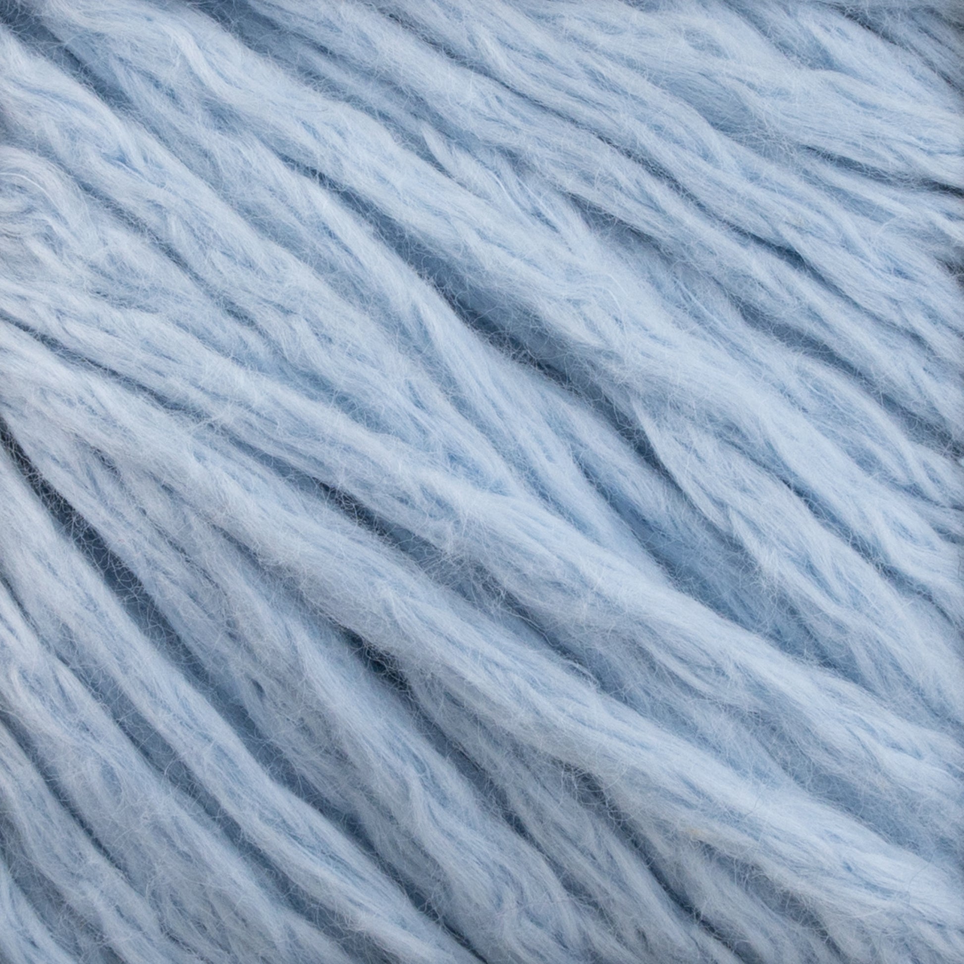 Close-up view of Cumulus Cotton by Juniper Moon Farm. The soft yarn is fluffy, with thick strands twisted together, creating a textured appearance. The color is a soft, pastel blue, giving the yarn a cozy and inviting look. Its durable chainette construction ensures lasting quality for all your projects. Available from Knitting Fever / Euro Yarns.