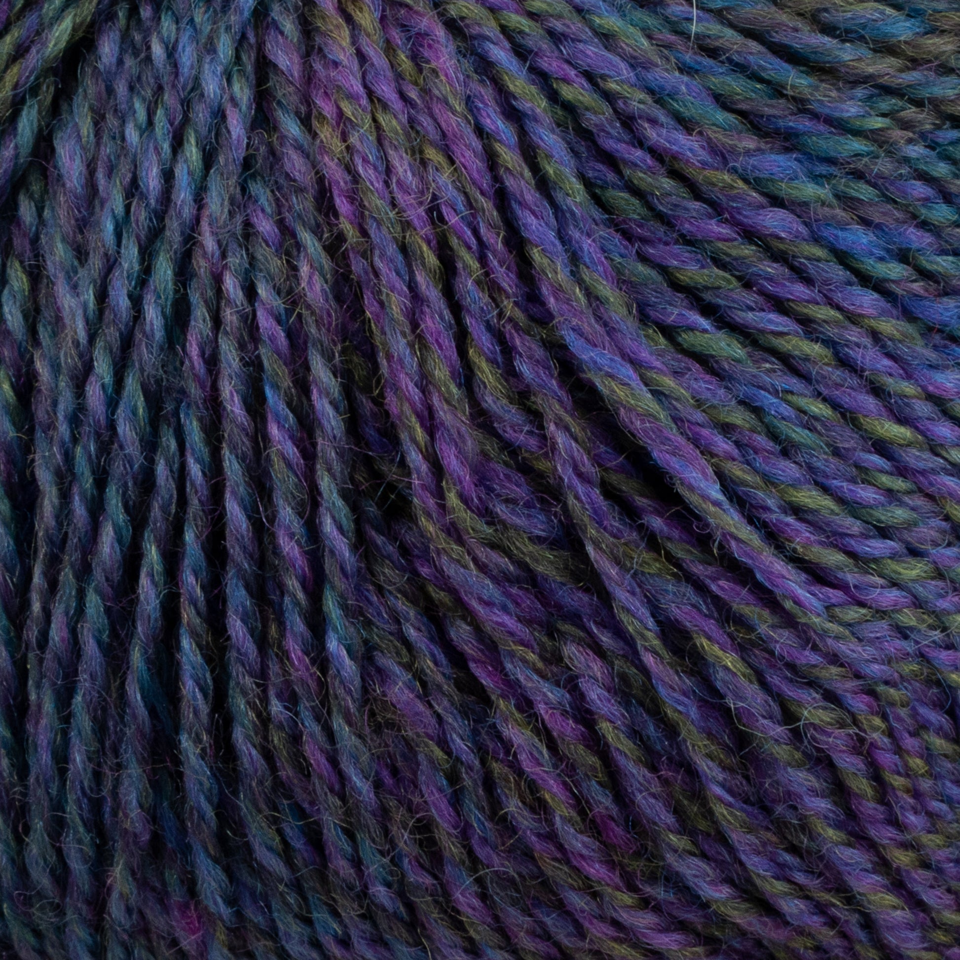 Close-up of a skein of Knitting Fever Painted Desert Yarn by Knitting Fever / Euro Yarns. The super fine weight yarn is twisted and showcases a rich blend of hues, predominantly blues, purples, and greens with long color changes that create a gradient effect. The texture appears soft and slightly fuzzy, suggesting it is likely made of wool or a wool blend.