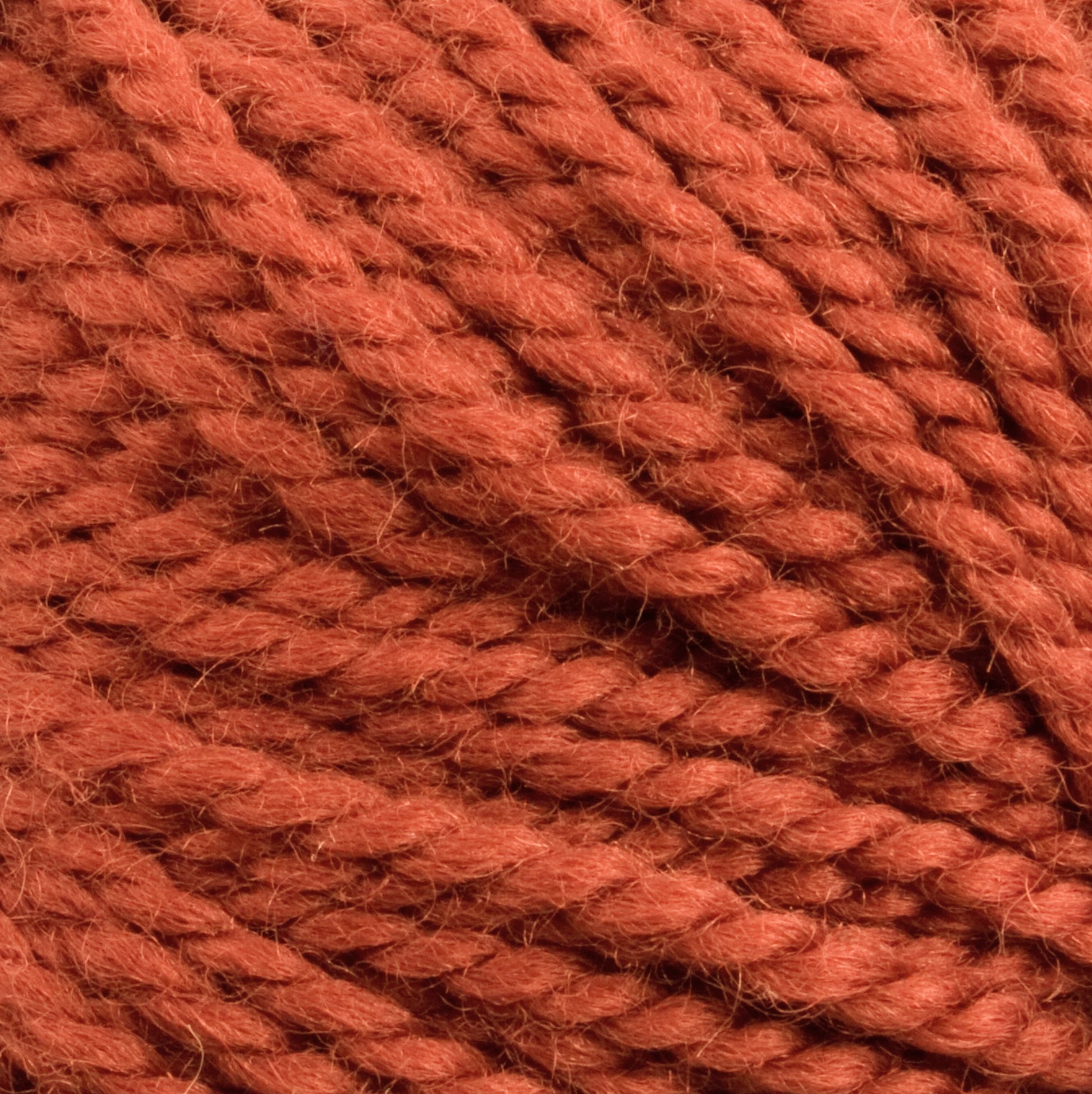 Close-up of a ball of soft, thick Norumbega yarn from Caledonian Dye Works in a rich, warm reddish-brown color. The texture displays various intertwined strands of 100% U.S. wool, highlighting the material's fluffiness and slight fuzziness.