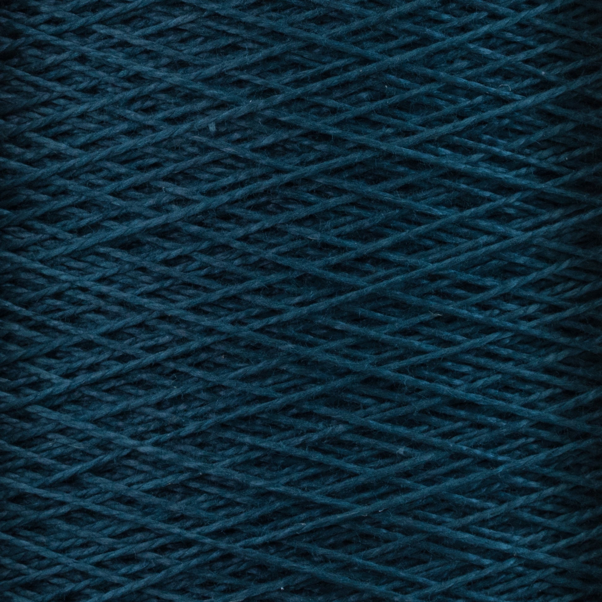 Close-up view of the Supreme Corp. 10/2 Pearl Cotton Yarn | Mini-cone in dark teal, showcasing its detailed, intertwined strands forming a textured pattern. The image highlights the rich colorfastness and intricate crisscrossing arrangement of these versatile fibers.