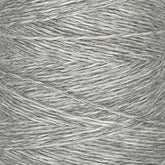 Close-up image of a spool of Jagger Brothers, Inc. JaggerSpun Heather 3/8 yarn. The light gray, worsted spun wool yarn is wound tightly around the spool, showcasing a variegated texture and slightly uneven threads. The overall appearance is soft, featuring a blend of light and darker gray tones reminiscent of heather yarns.