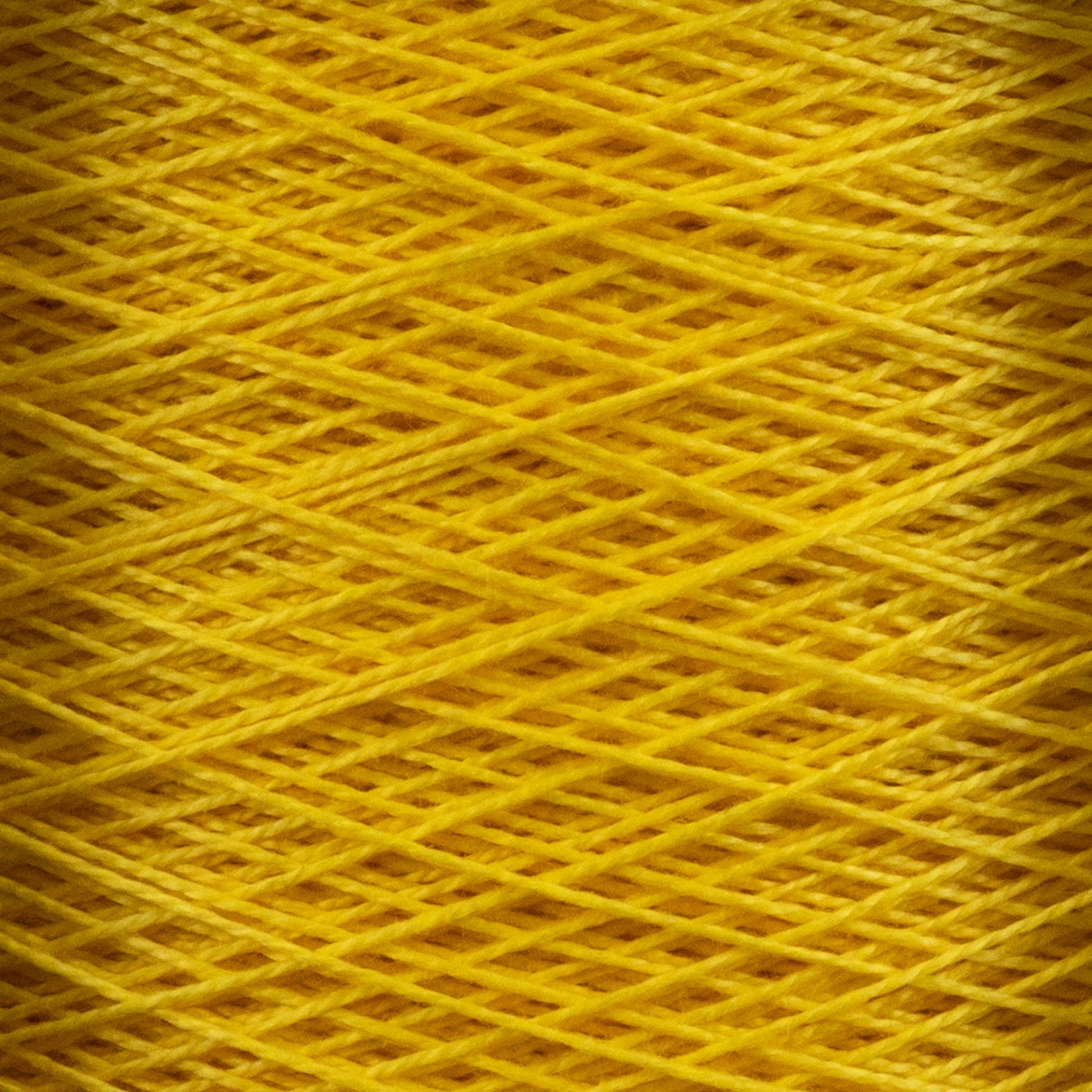 Close-up view of bright yellow 10/2 Pearl Cotton Yarn | Mini-cone by Supreme Corp. wound tightly in crisscross patterns, forming a textured surface. The intricate overlapping threads create a vibrant and uniform appearance, showcasing the versatility and colorfastness of the yarn.