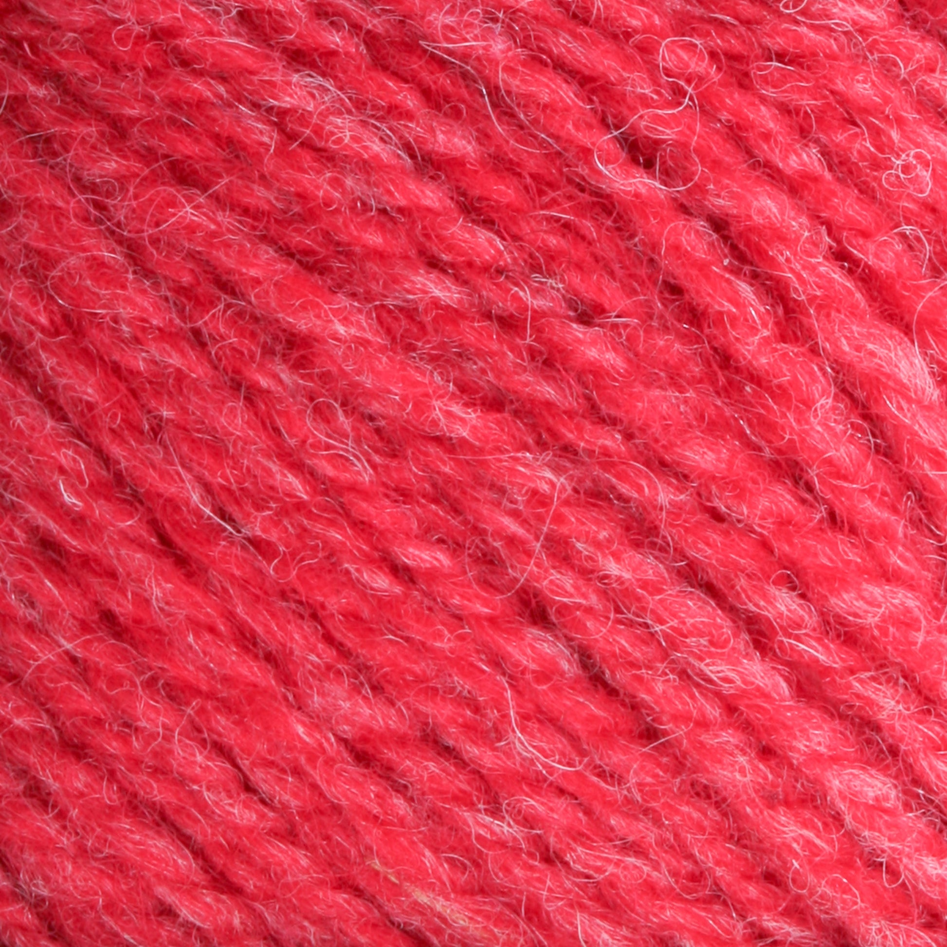 Close-up of Bartlettyarns Maine Wool Yarn with some white fibers woven into the red strands. The texture appears soft and slightly fuzzy, emphasizing the intricate detail, heathered colors, and artisanal quality of the material.