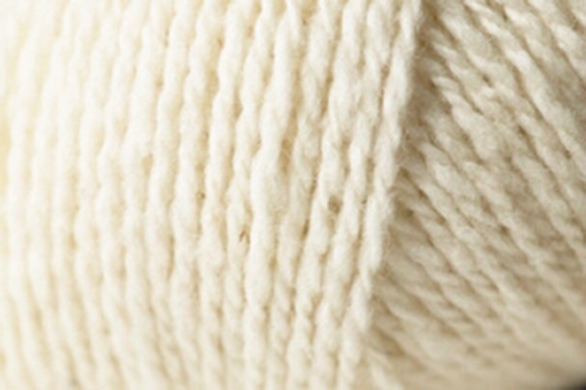 Close-up view of a soft, cream-colored Jo Sharp Silkroad DK Tweed yarn ball from Kingfisher Yarn & Fibre, showcasing its texture and tightly wound fibers.