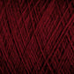 Close-up of JaggerSpun Maine Line 3/8 Yarn in maroon, manufactured by Jagger Brothers, Inc. The worsted spun yarn is tightly wound, forming an intricate pattern of overlapping strands. The texture looks soft and slightly fuzzy, with varying shades of red visible under the lighting.