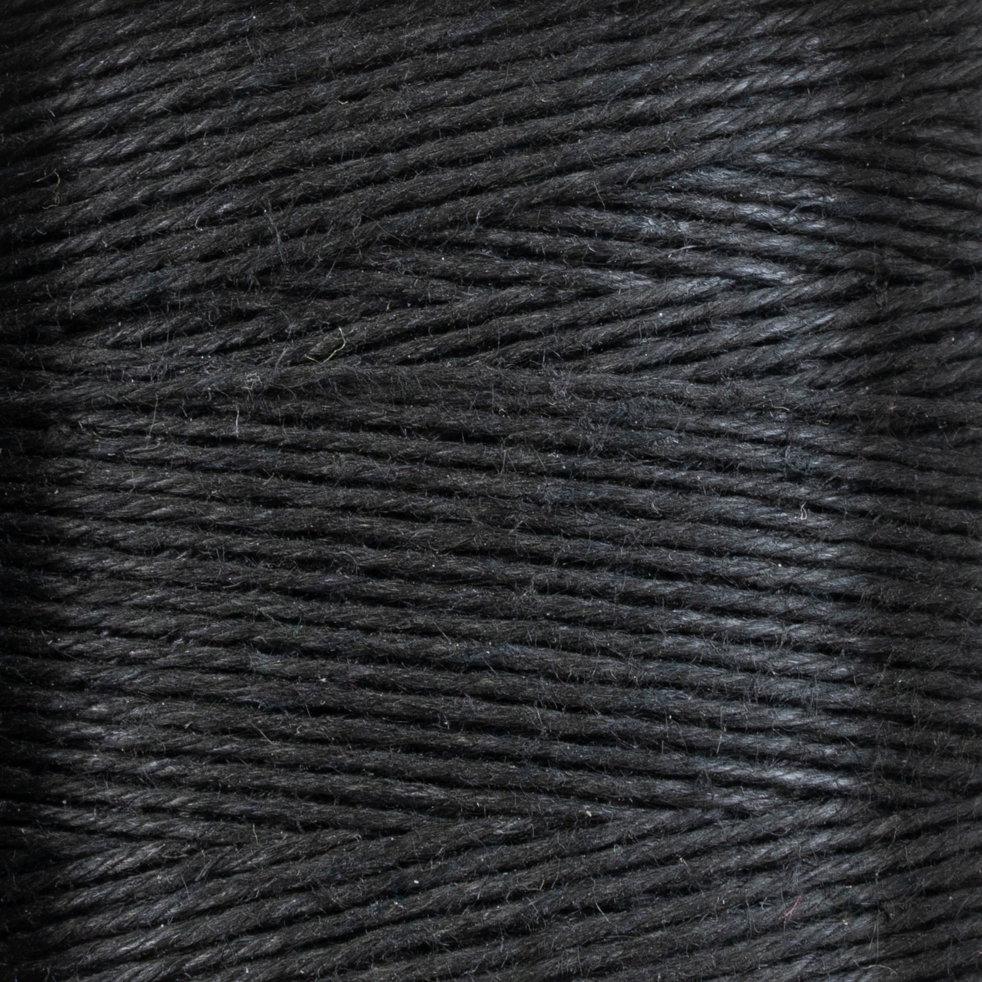 Close-up of Stuart C. Hurlbert & Co.'s 16/5 Linen Rug Lacing (Black) tightly wound into a tube. The fibers exhibit a slight gloss, creating nuanced highlights and shadows on the surface. The texture appears smooth and consistent throughout, showcasing both the sleekness and strength ideal for crafting heavy rugs.