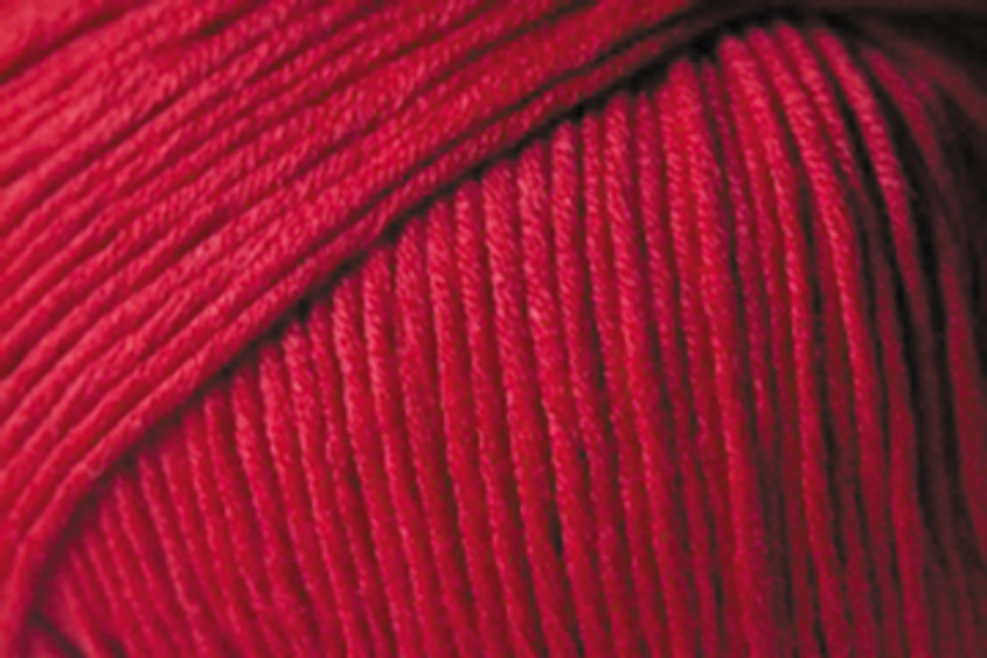 Close-up image of a ball of vibrant red yarn. The strands, made from Jo Sharp Soho Summer DK Cotton by Kingfisher Yarn & Fibre, are neatly wound, showcasing the texture and individual fibers. This lightweight cotton yarn dominates the image with its brilliant hue.