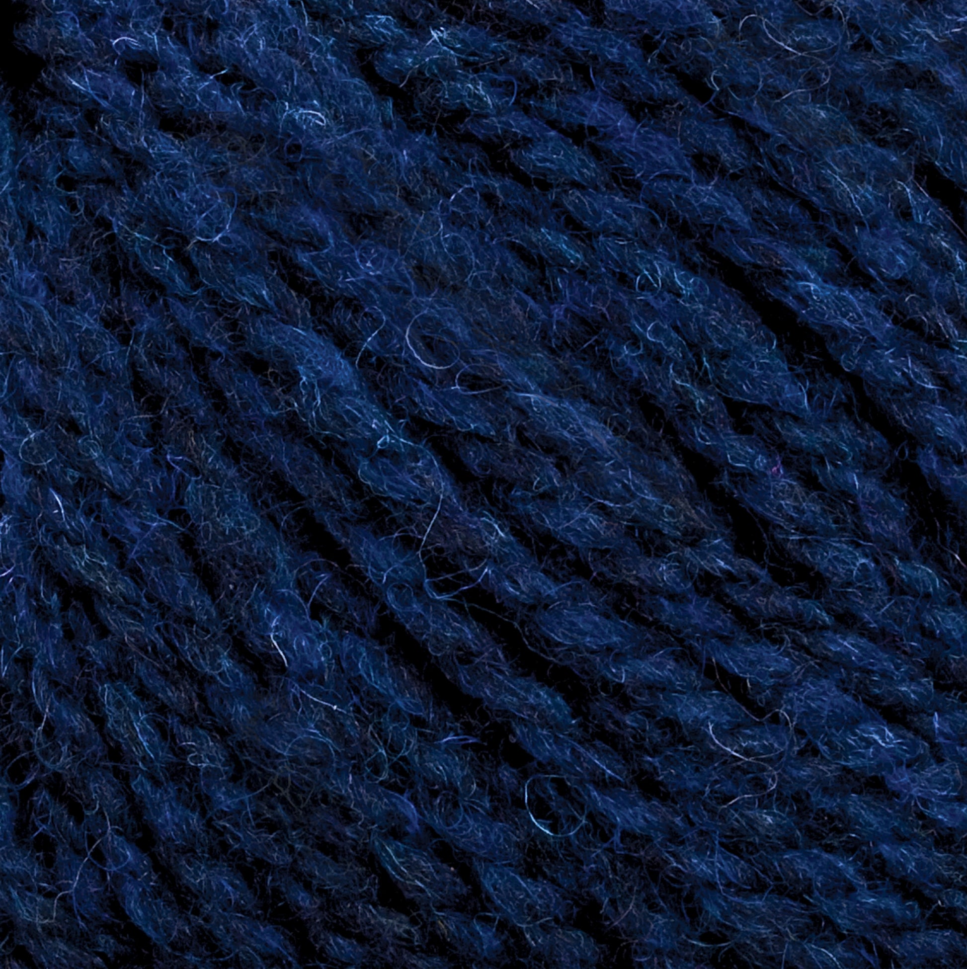 Close-up image of dark blue Harrisville Designs Harrisville Shetland Yarn - Unwashed Cones, showcasing its soft and fuzzy texture with intertwined fibers. The yarn appears thick and woolly, perfect for Fair Isle knitting designs, creating a rich and slightly uneven surface.