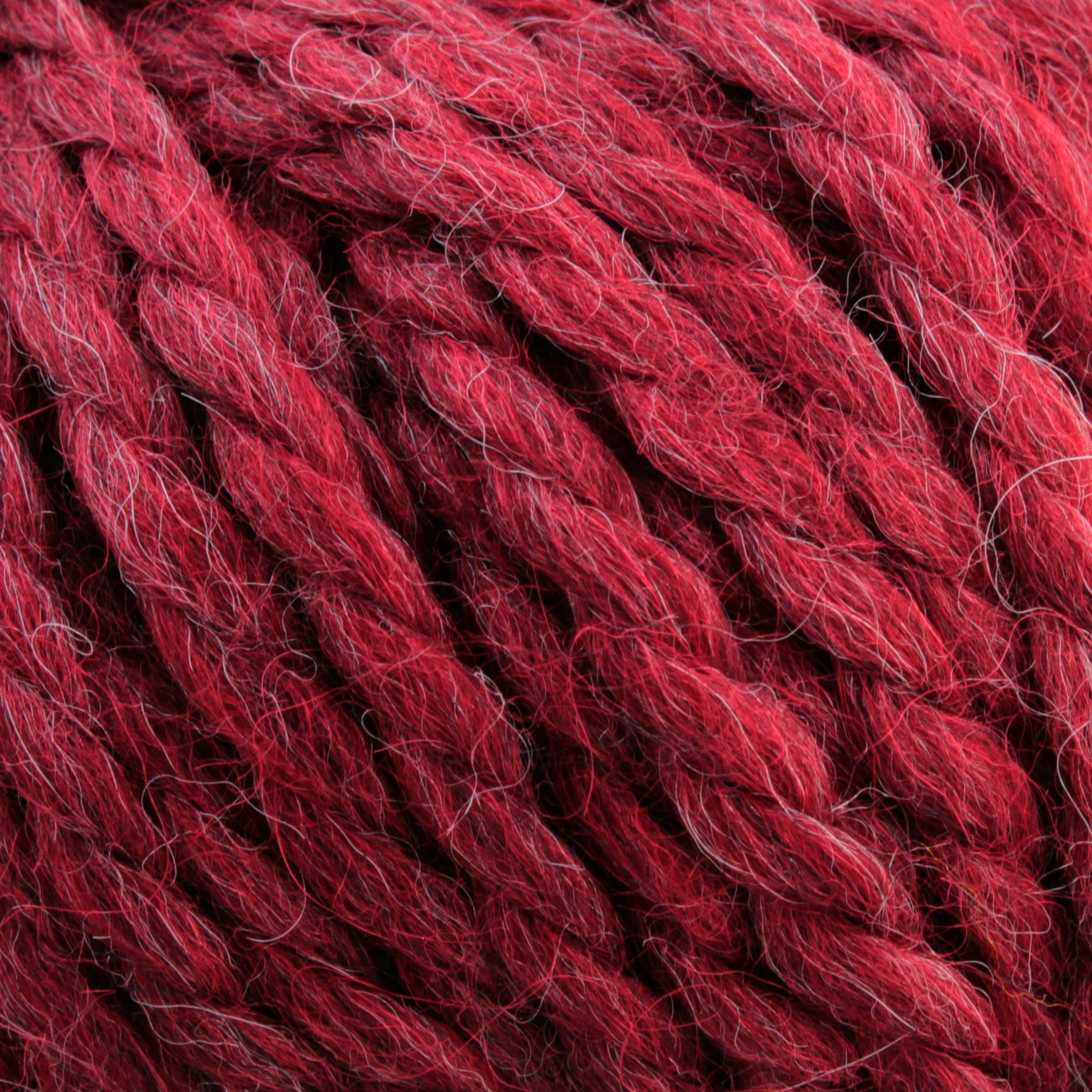 Close-up of thick, red strands of Baby Alpaca Grande by Plymouth, twisted together. This bulky weight yarn from Plymouth Yarn Co. features a slightly fuzzy texture with hints of different shades of red, giving it a rich, ultra-soft multi-dimensional appearance.