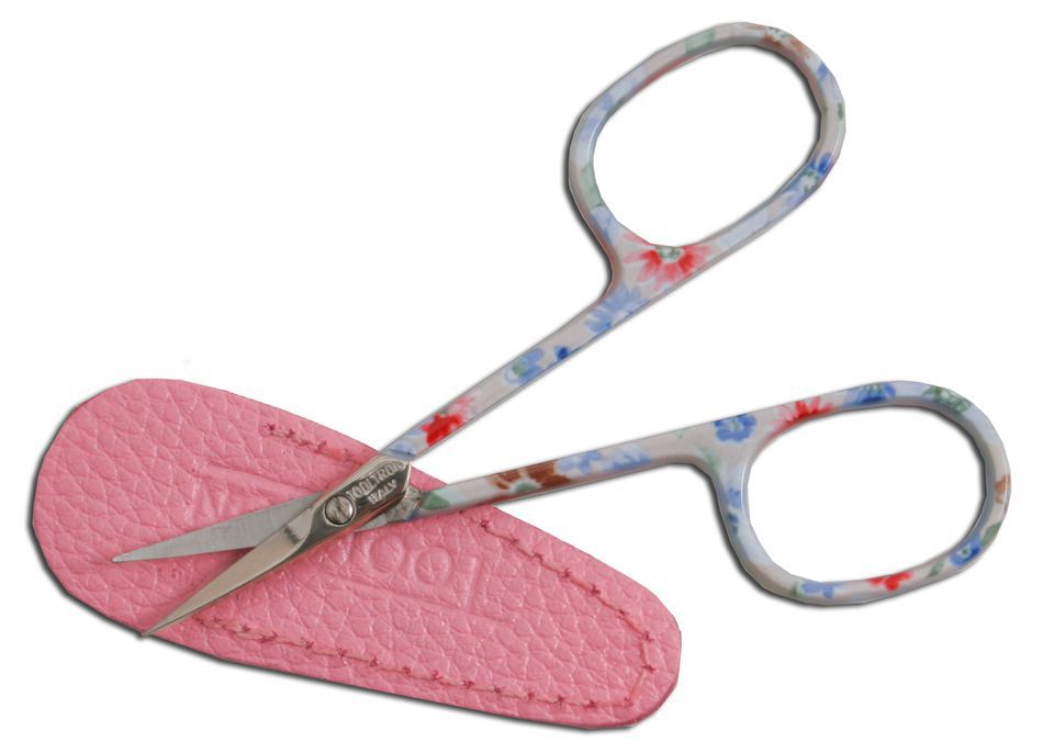 A pair of small, silk-screened Floral Scissors with curved tips from Tool Tron Industries, featuring a vibrant mix of red, blue, and green flowers on the handles and blades, rests open on a pink faux-leather sheath.