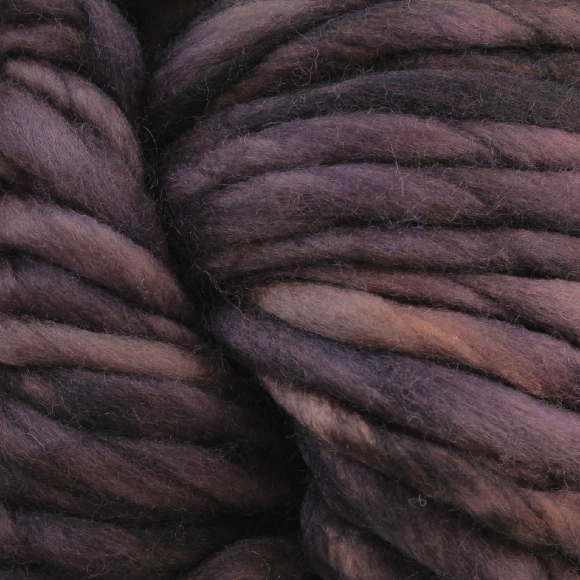 Close-up image of Malabrigo Yarn's Malabrigo Rasta chunky, twisted wool yarn in varying shades of purple and brown, showcasing its soft, fibrous texture and slight sheen. Some individual strands are visible, highlighting the super bulky yarn's thick and cozy appearance, perfect for quick-to-knit projects.