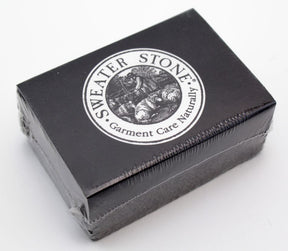 A black rectangular box labeled "Sweater Stone - Made in USA" with the tagline "Garment Care Naturally." The label features a circular logo depicting a person working with a stone. Designed for superior fabric care, the pumice surface revitalizes garments. The box is shrink-wrapped in plastic.