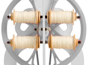 A close-up view of the Schacht Ladybug Lazy Kate shows four bobbins loaded with spun white yarn. The bobbins are evenly distributed and symmetrically arranged on the frame, which features circular cutouts. This product by Schacht Spindle Co. appears to be well-maintained and functional.