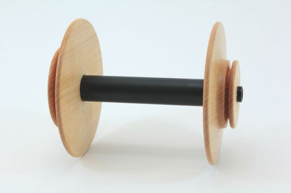 The Schacht Spinning Wheel Bulky Bobbin by Schacht Spindle Co. features two light-colored wooden discs on either end, connected by a black cylindrical shaft, all set against a plain white background.