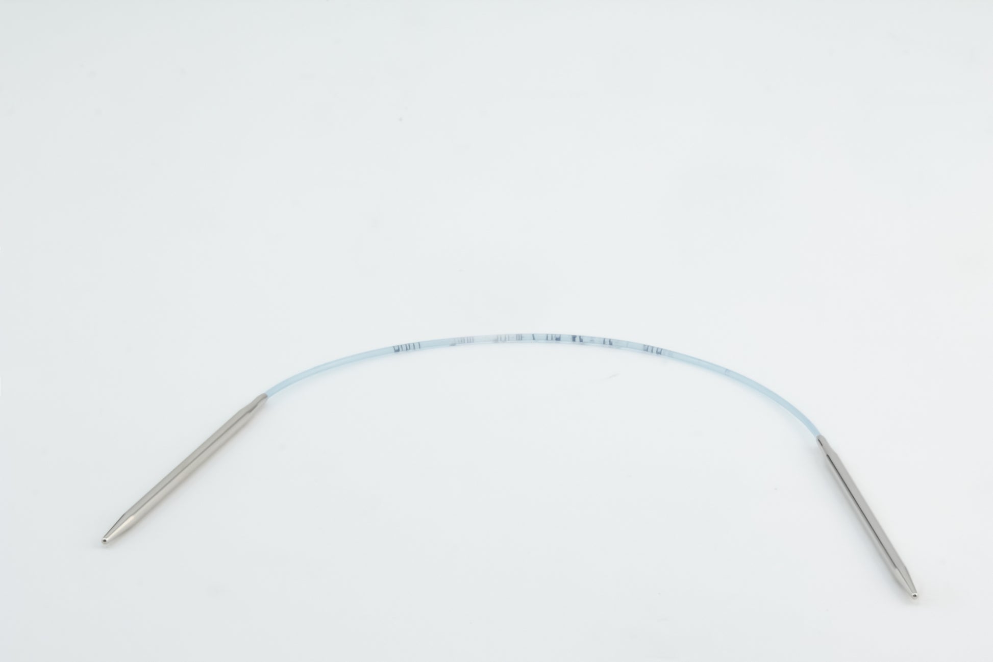 A medical device featuring a flexible, transparent tube with metal connectors at both ends, placed on a plain white background. The tube includes printed measurements or markings along its length, reminiscent of the precision found in Skacel's Addi Turbo Circular Knitting Needles.